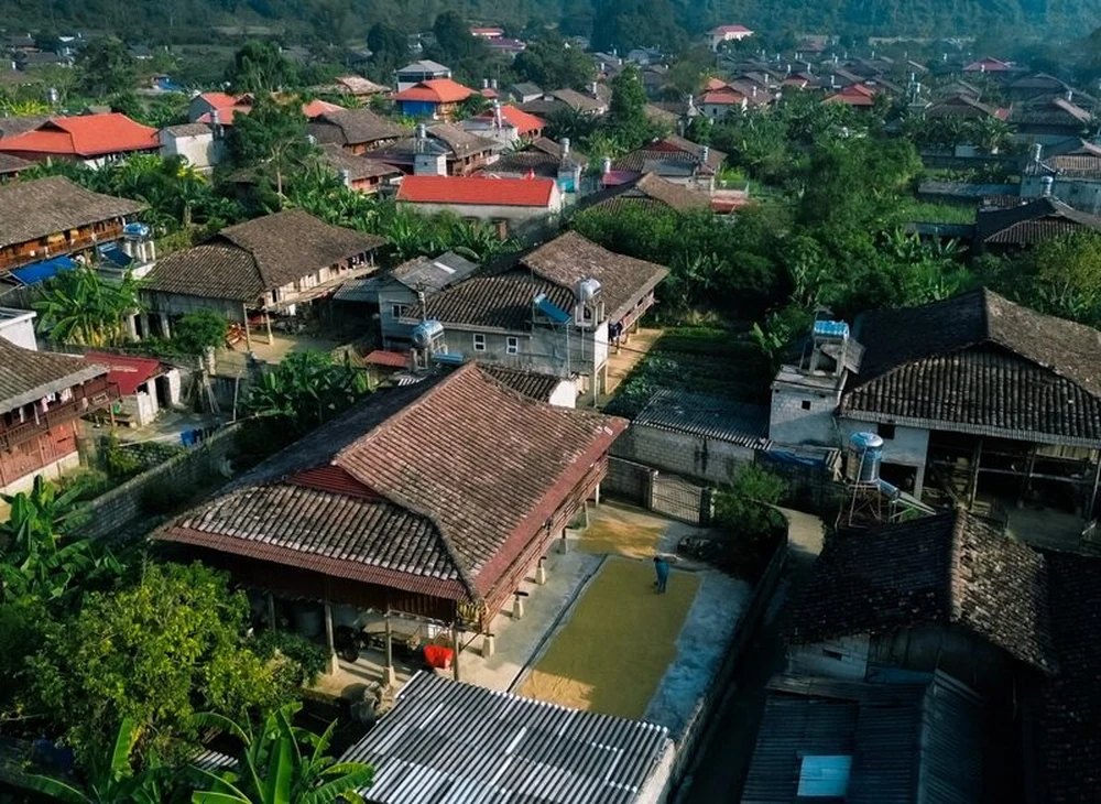 Les toits de tuiles traditionnels du village de Quỳnh Sơn vus du haut, avec un habitant étalant le riz à sécher dans la cour d'une maison sur pilon.