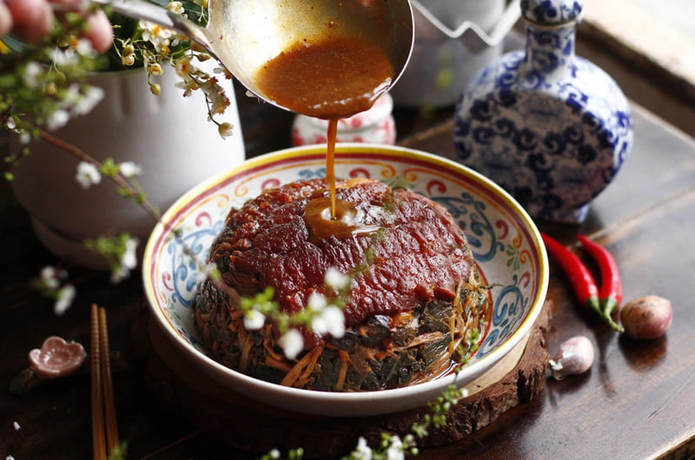 Préparation du khau nhục, une spécialité culinaire renommée du peuple Tày à Quỳnh Sơn, avec une louche versant de la sauce parfumée sur la viande.