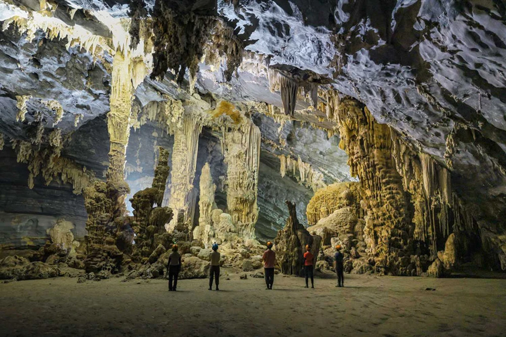 Spéléologues admirant d'impressionnantes colonnes de stalactites et stalagmites à l'intérieur du système de grottes de Tu Lan.
