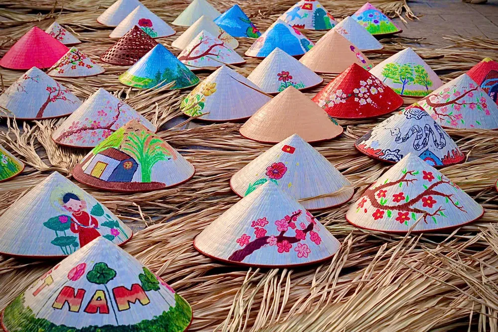 Des chapeaux coniques colorés et peints à la main séchant sur de la paille dans le village artisan de Tri Lễ.