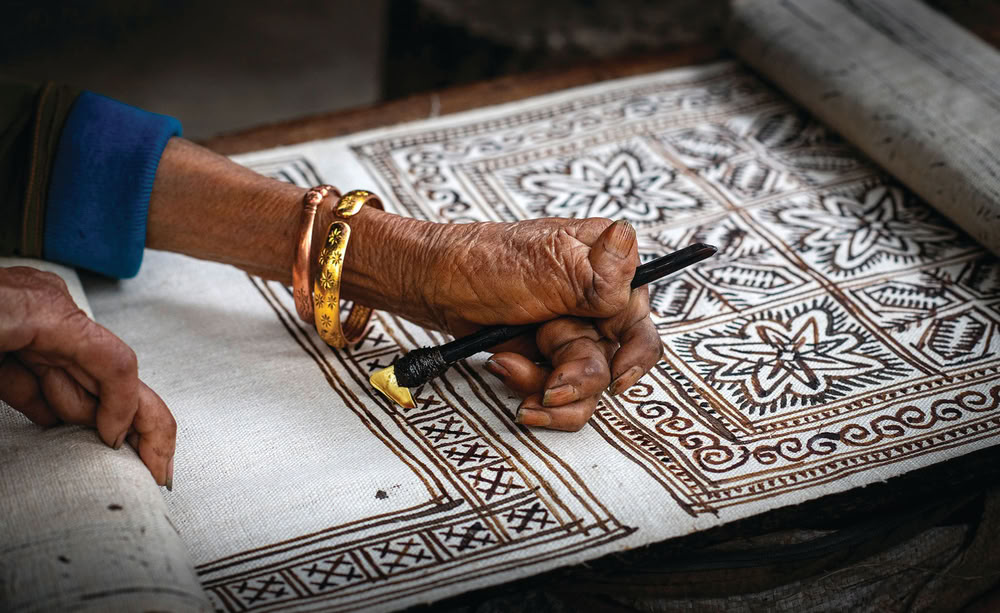 Main traçant des motifs géométriques à la cire.